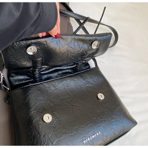 Detail view of the black textured crossbody bag showing dual magnetic buckles and logo