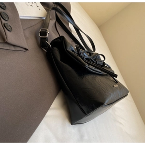 Detail of black pleated crossbody bag featuring side metal logo and top drawstring bow