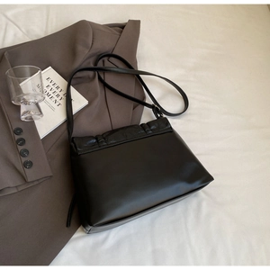Detail of black crossbody bag with crocodile embossed leather flap on a neutral background