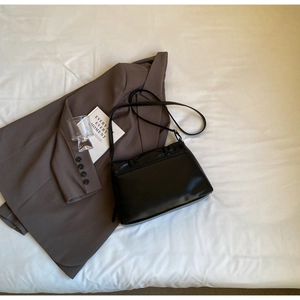 Detail of black ballet style crossbody bag with pleated cover on office wear blazer