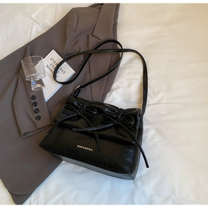 Detail of black glossy leather shoulder bag with chic bow accents and elegant pleats