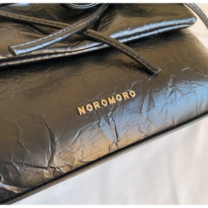Detail of black wrinkled leather texture and golden metal logo on the ballet style bag