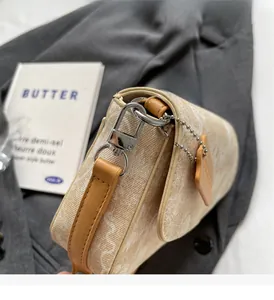 Detail of light beige canvas shoulder bag featuring brown leather strap and silver hardware