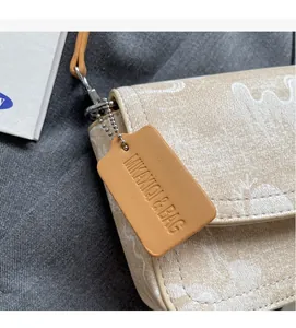 Detail of floral canvas handbag featuring a brown leather brand tag and silver chain