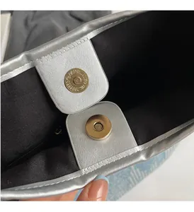 Detail of silver metallic leather trim and golden magnetic snap closure on canvas tote bag