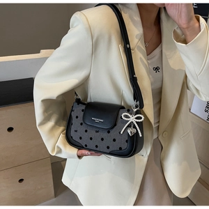 Detail of grey polka dot shoulder bag with pearl bow charm and black leather flap