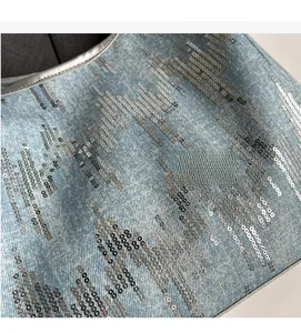 Detail of light blue washed denim fabric with silver sequins and grey piping trim