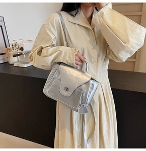 Détail du sac à main argenté avec pendentif cœur et fermoir rotatif sur manteau beige