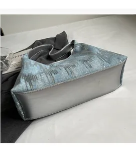 Close-up detail of light blue denim shoulder bag with silver sequins and metallic trim
