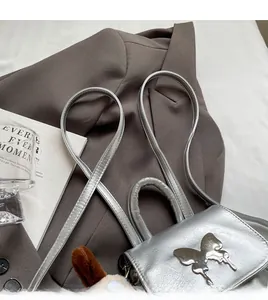 Détail du mini sac argenté métallisé avec boucle papillon sur fond de blazer marron