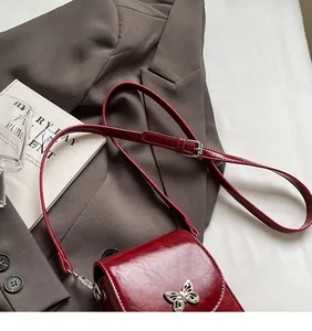 Detail of burgundy crossbody phone bag with silver butterfly buckle and leather texture