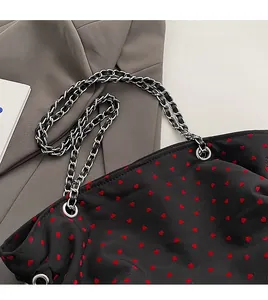 Detail of silver chain strap and red heart patterns on a black fabric tote bag