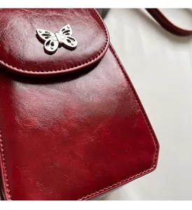 Detail of burgundy leather crossbody phone bag featuring a silver butterfly metal clasp