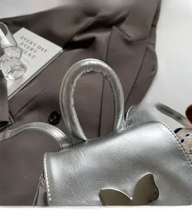Détail du sac à dos en cuir argenté avec boucle papillon métallique et poignée rembourrée