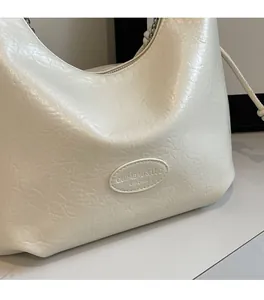 Vista macro dettagliata della trama in pelle crema e logo goffrato sulla borsa hobo