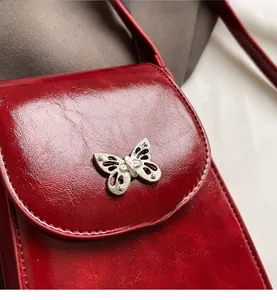 Close-up of red PU leather phone bag featuring a delicate silver butterfly pendant detail