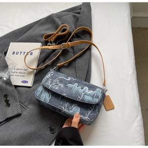 Detailed embroidery of white pine trees on blue denim flap bag with adjustable brown strap
