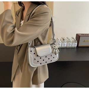 Close-up of silver polka dot underarm bag with a pearl bow charm on a blazer model