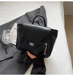 Détail de la texture cuir noir mat et du charme de chaîne en forme de cœur sur le sac