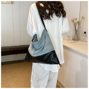 Detail of a large denim and leather tote bag worn by a model in a minimalist room