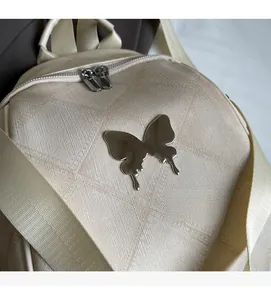 Detail of beige backpack featuring textured fabric and a silver butterfly metal ornament