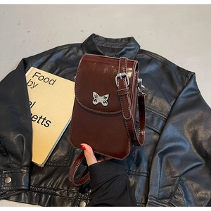 Detail of a dark brown glossy patent leather crossbody phone bag with silver butterfly buckle