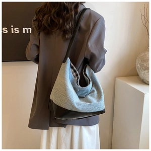 Detail of denim and leather tote bag with plaid lining shown on a model's shoulder