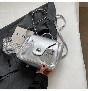 Détail du sac à main en cuir argenté avec poche cœur et chaîne sur blazer gris