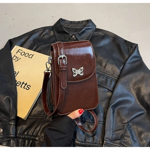 Close-up of brown oiled leather phone bag with silver butterfly charm and adjustable strap