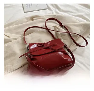 Detail of dark red glossy PU leather shoulder bag with a bow decoration and strap