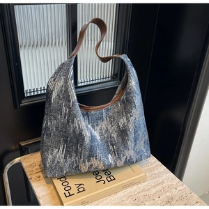 Detail of blue sequined denim hobo bag with brown leather strap on decorative books