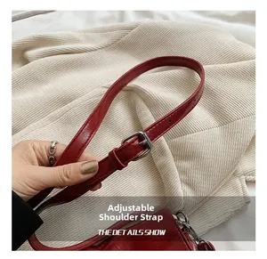 Detail of adjustable shoulder strap with silver buckle on dark red pleated bucket bag