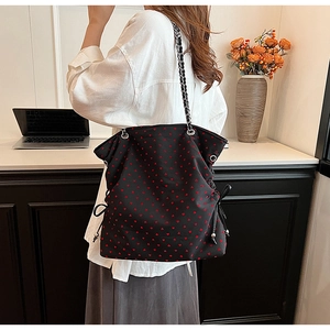 Detail of large black tote bag with red heart pattern and metal chain strap