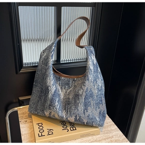 Close-up of blue denim hobo bag with silver sequins and brown leather strap detail