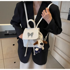 Détail du sac à dos blanc en PU avec boucle papillon argentée et charm chien en peluche
