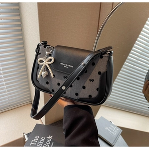 Detail of grey polka dot fabric with bow embroidery and pearl heart charm on a flap bag