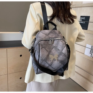Rear view of a grey quilted backpack with silver butterfly detail worn on a white blazer