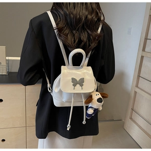 Gros plan du mini sac à dos blanc avec boucle papillon argentée et porte-clés peluche