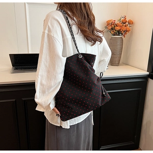 Detail of large black tote bag with red heart pattern and metal chain strap on a desk