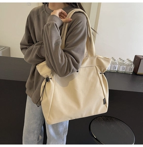 Detail of beige canvas tote bag showing black side drawstring and textured fabric