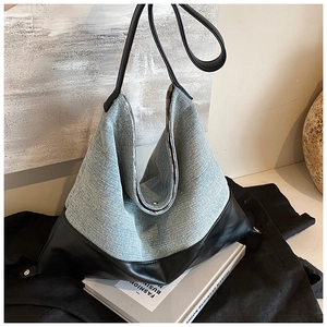 Detail of blue denim and black leather patchwork large shoulder bag on fashion books
