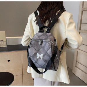 Detail of grey quilted backpack with white butterfly charm on woman's back