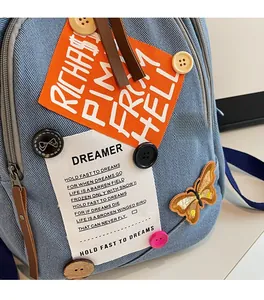 Detailed close-up of light blue denim backpack with embroidery and vintage buttons