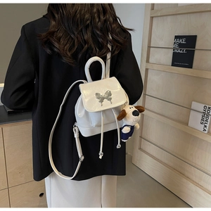 Détail d'un mini sac à dos en cuir verni blanc avec papillon argenté et breloque