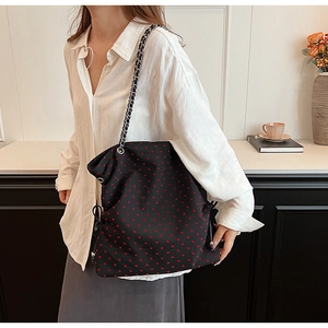 Detail of black tote bag featuring red heart prints and silver metal chain strap
