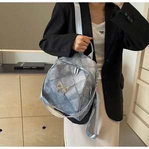 Detail of light blue quilted denim backpack featuring a 3D metal butterfly accent