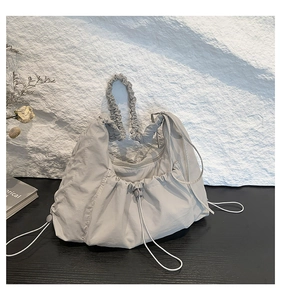 Detail of light grey pleated nylon tote bag with drawstring closure on textured stone