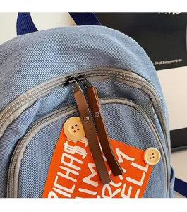 Detail of light blue corduroy backpack featuring orange patch and metal rivet zippers