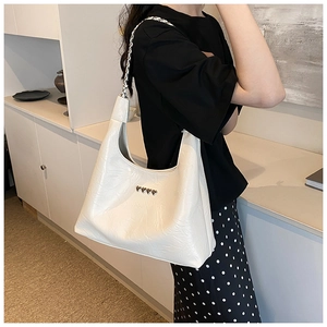 Close-up of white leather tote bag featuring heart rivets and silver chain strap
