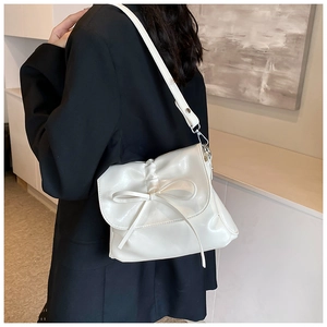 Detailed close-up of cream-white pleated handbag with a ribbon bow and glossy PU leather